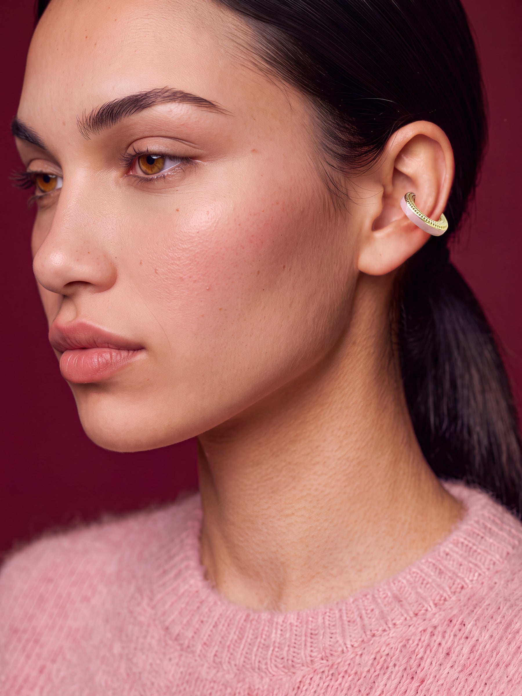Blush Serenity gold-plated ear cuff with powder pink enamel, model in a pink sweater on a burgundy backdrop