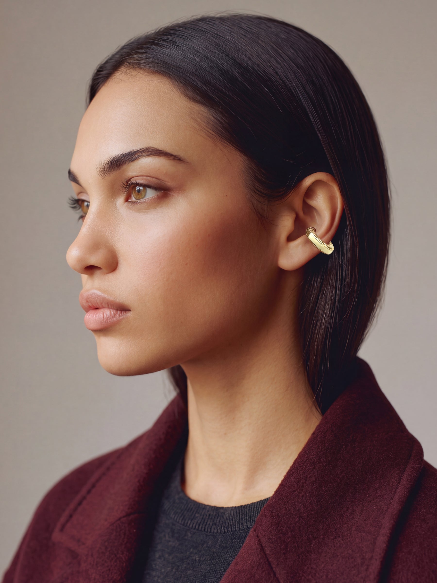 Hola Aura gold-plated ear cuff on a model in a burgundy coat, profile view