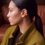 Ignite Pulse silver ear cuff with orange enamel on a model in an olive coat, profile view