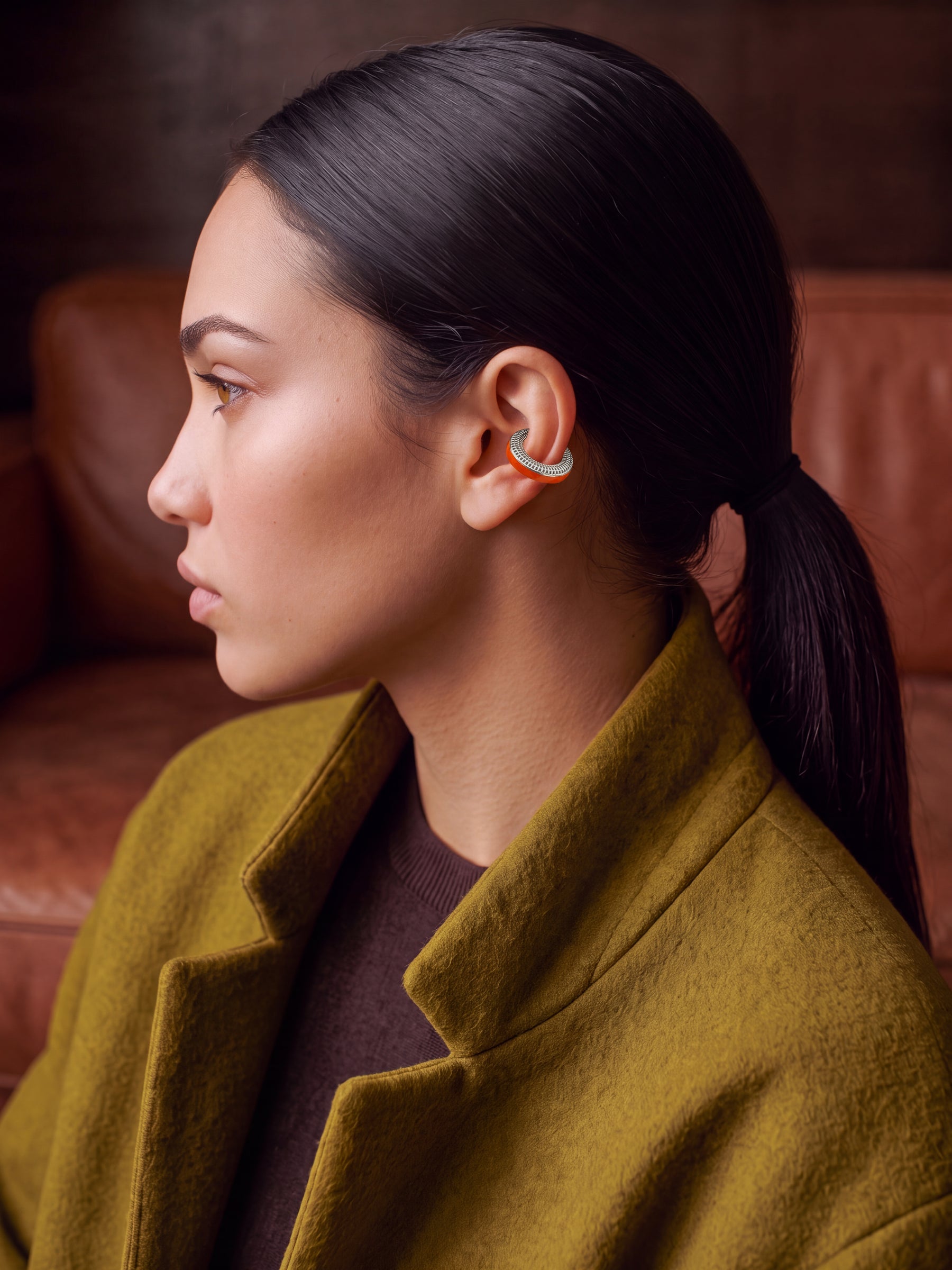 Ignite Pulse silver ear cuff with orange enamel on a model in an olive coat, profile view