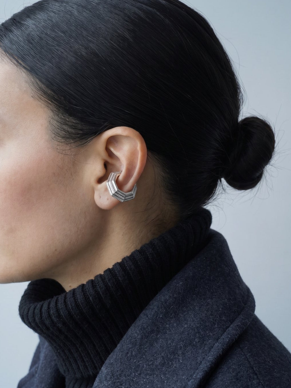 Model wearing the Octa Ear Cuff with a charcoal wool coat and black turtleneck, editorial shot