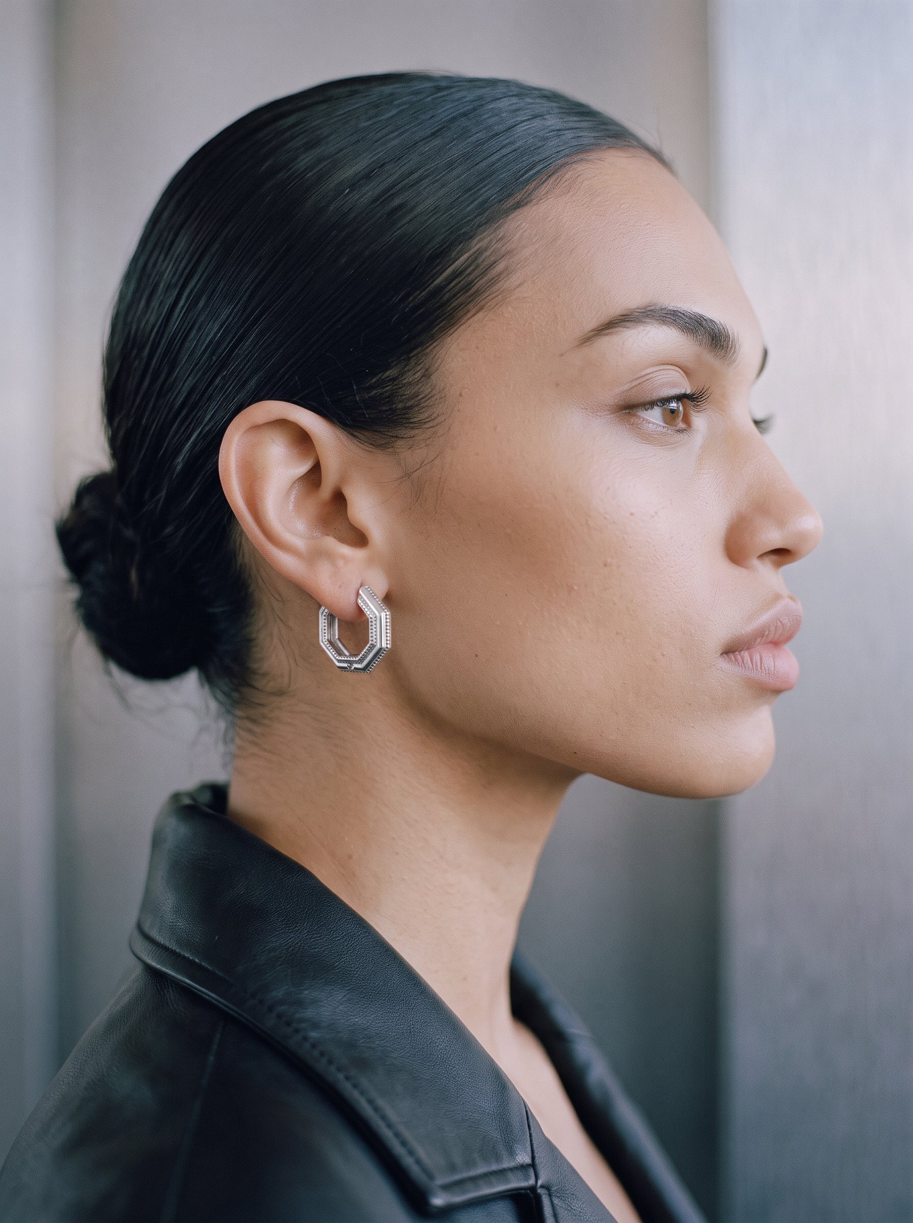 Model wearing Octa earrings in profile, rhodium-plated 925 sterling silver octagonal hoop, black leather jacket
