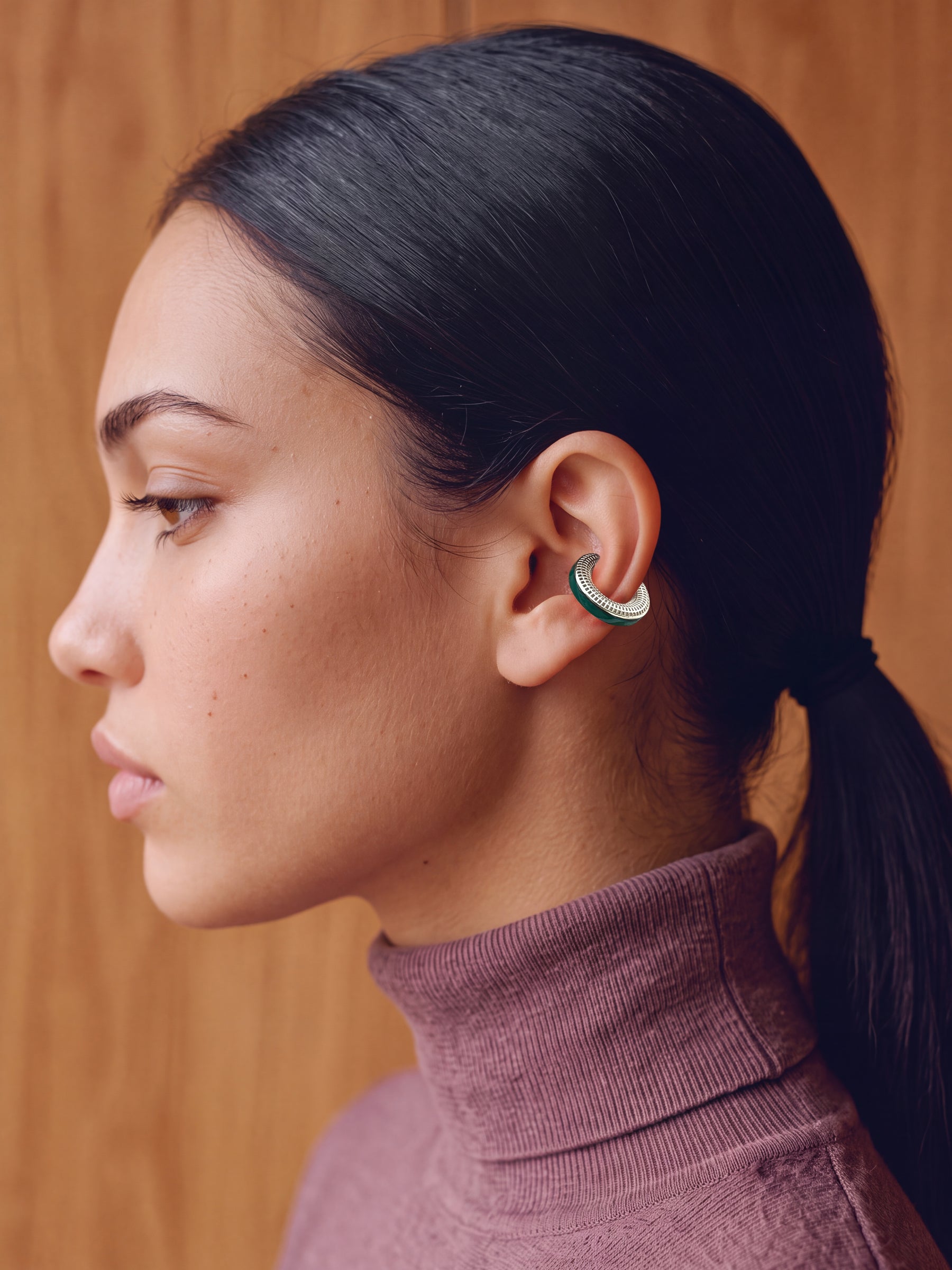Model wearing the Verdant Poise silver ear cuff with green enamel and a plum turtleneck, profile view